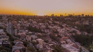 Aerial view of a Adelaide residential suburb at sunset, with homes and winding streets in the foreground and the city skyline in the distance.