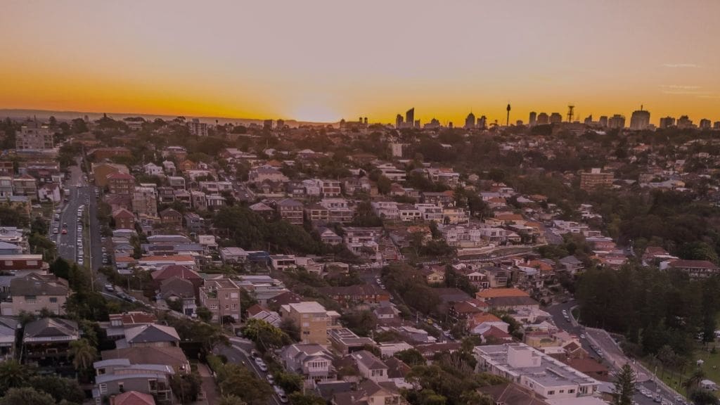 Aerial view of a Adelaide residential suburb at sunset, with homes and winding streets in the foreground and the city skyline in the distance.